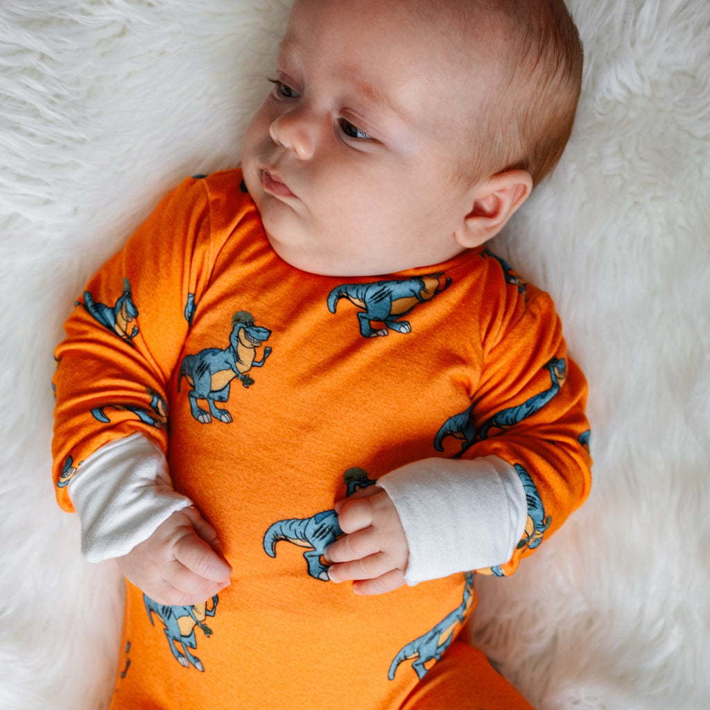 Baby wearing an orange onesie with dinosaur patterns on a white fluffy surface