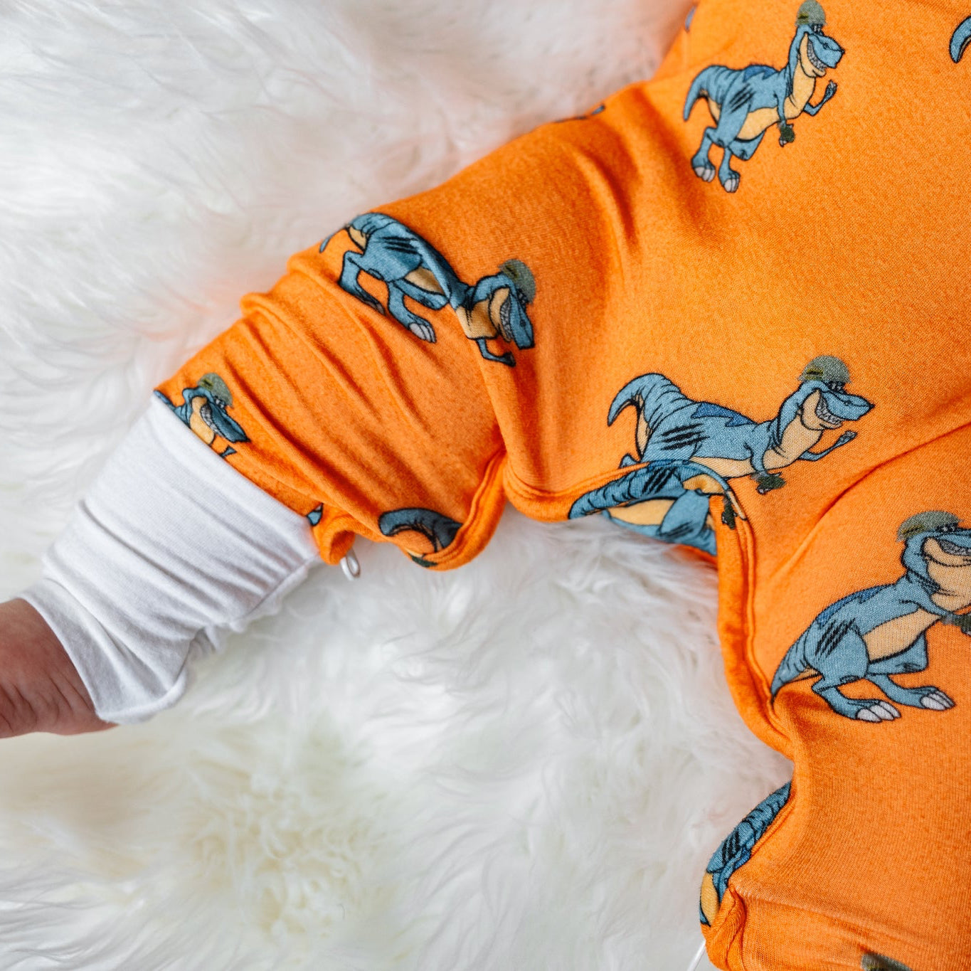 Orange baby onesie with dinosaur pattern on a white fluffy surface