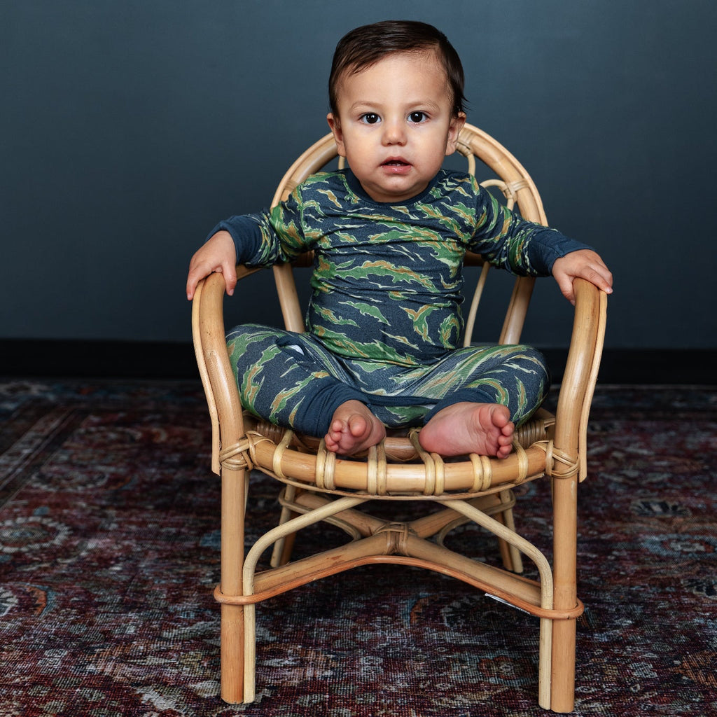 Baby in a camouflage outfit sitting on a small wooden chair against a dark background
