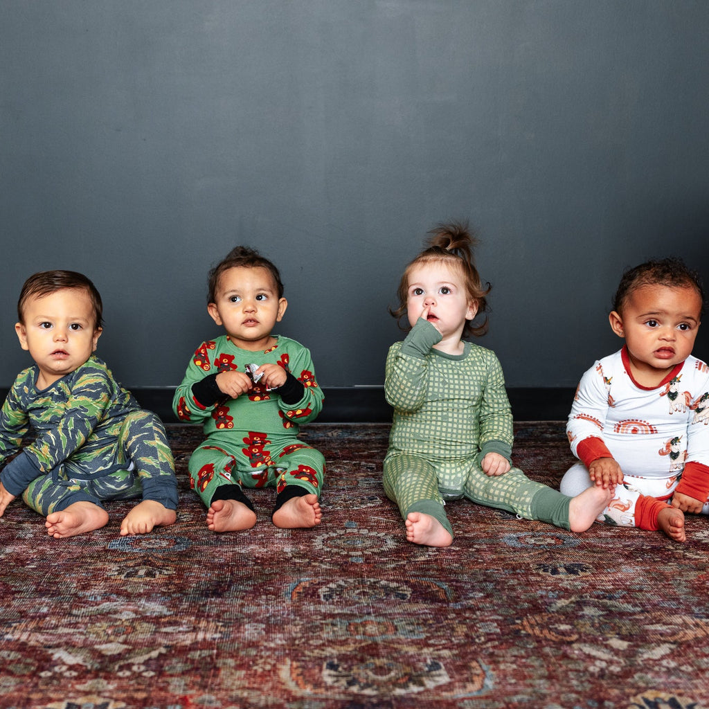 Four children in pajamas sitting on a patterned rug against a dark wall.