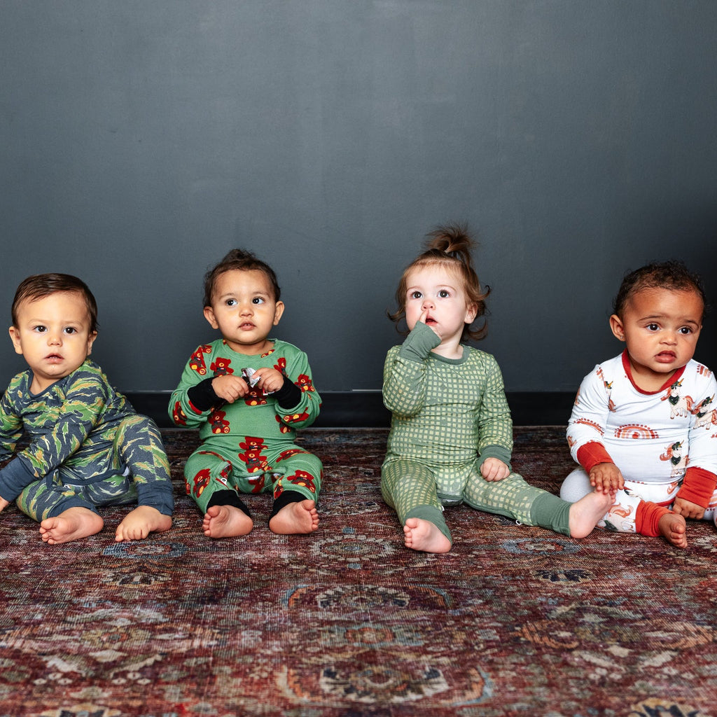 Four children in pajamas sitting on a patterned rug against a dark wall.