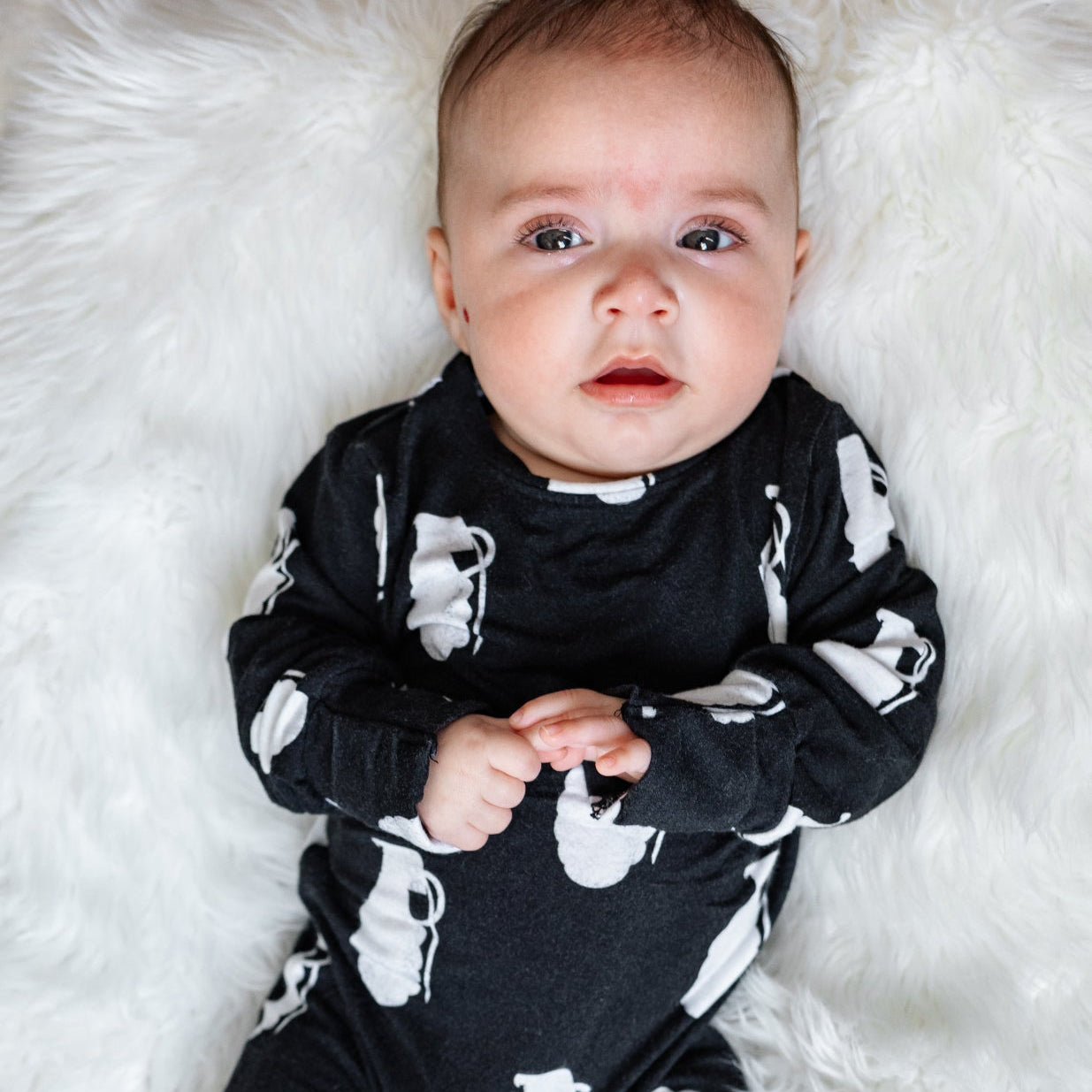 Baby wearing a black outfit with white patterns on a white fluffy surface
