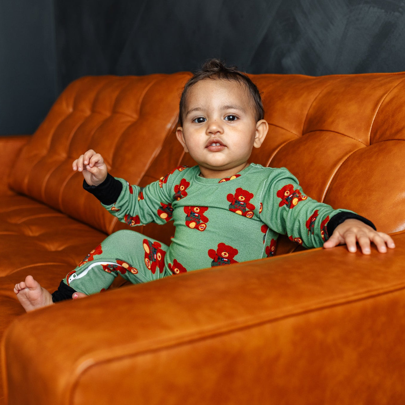 Child in a green floral outfit sitting on an orange couch.