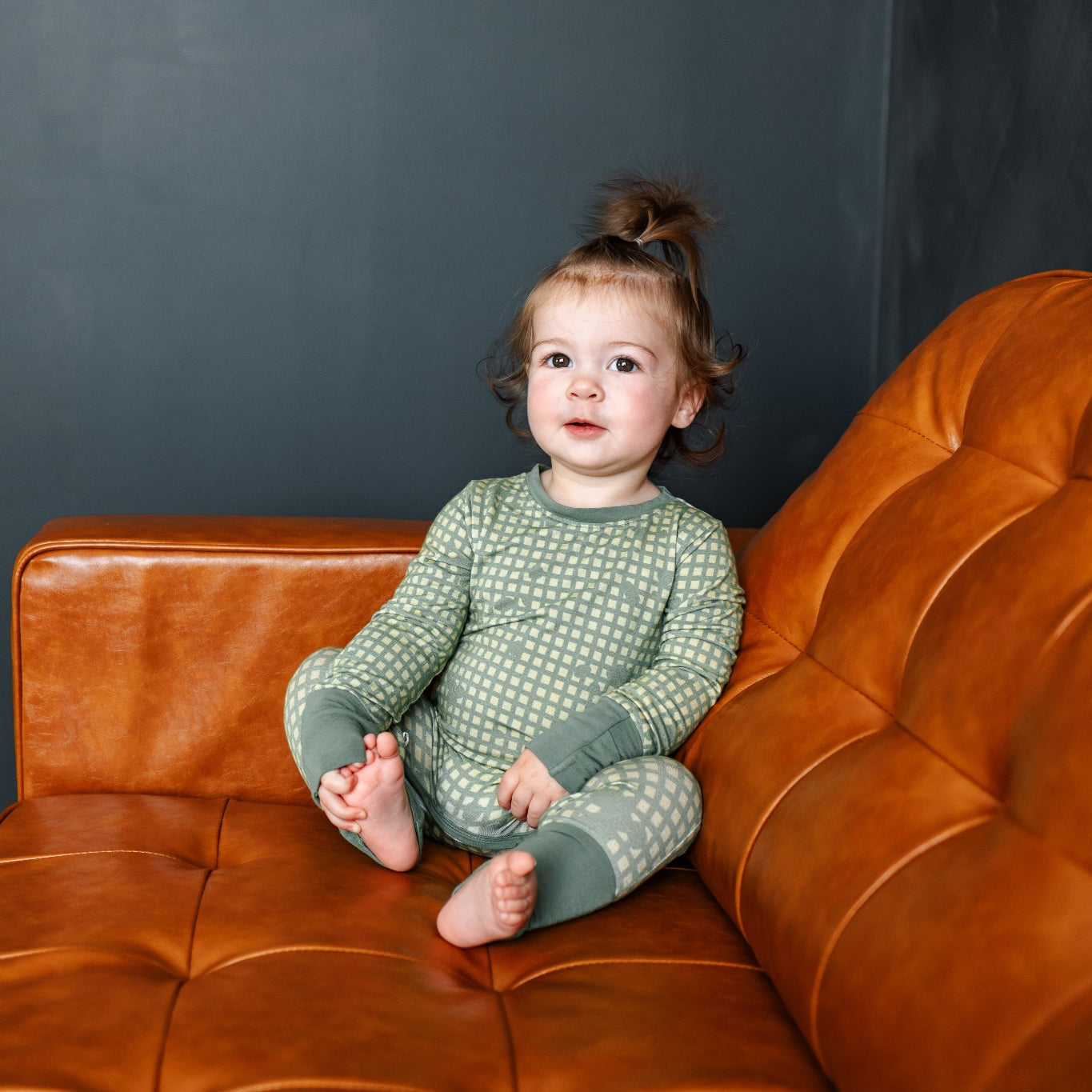 Child sitting on a brown leather couch against a dark gray wall