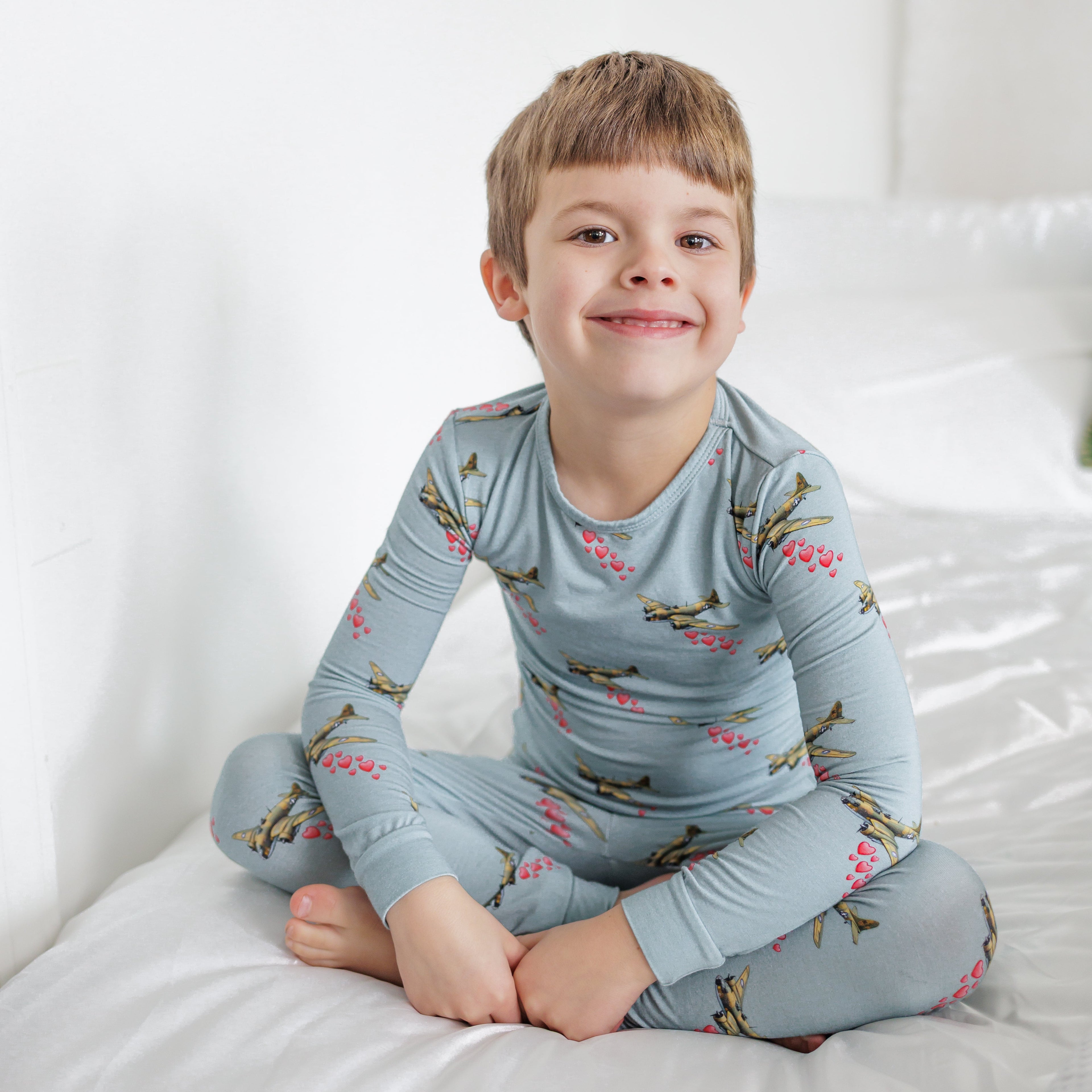 Child wearing a blue pajama set with airplane pattern on a white bed.