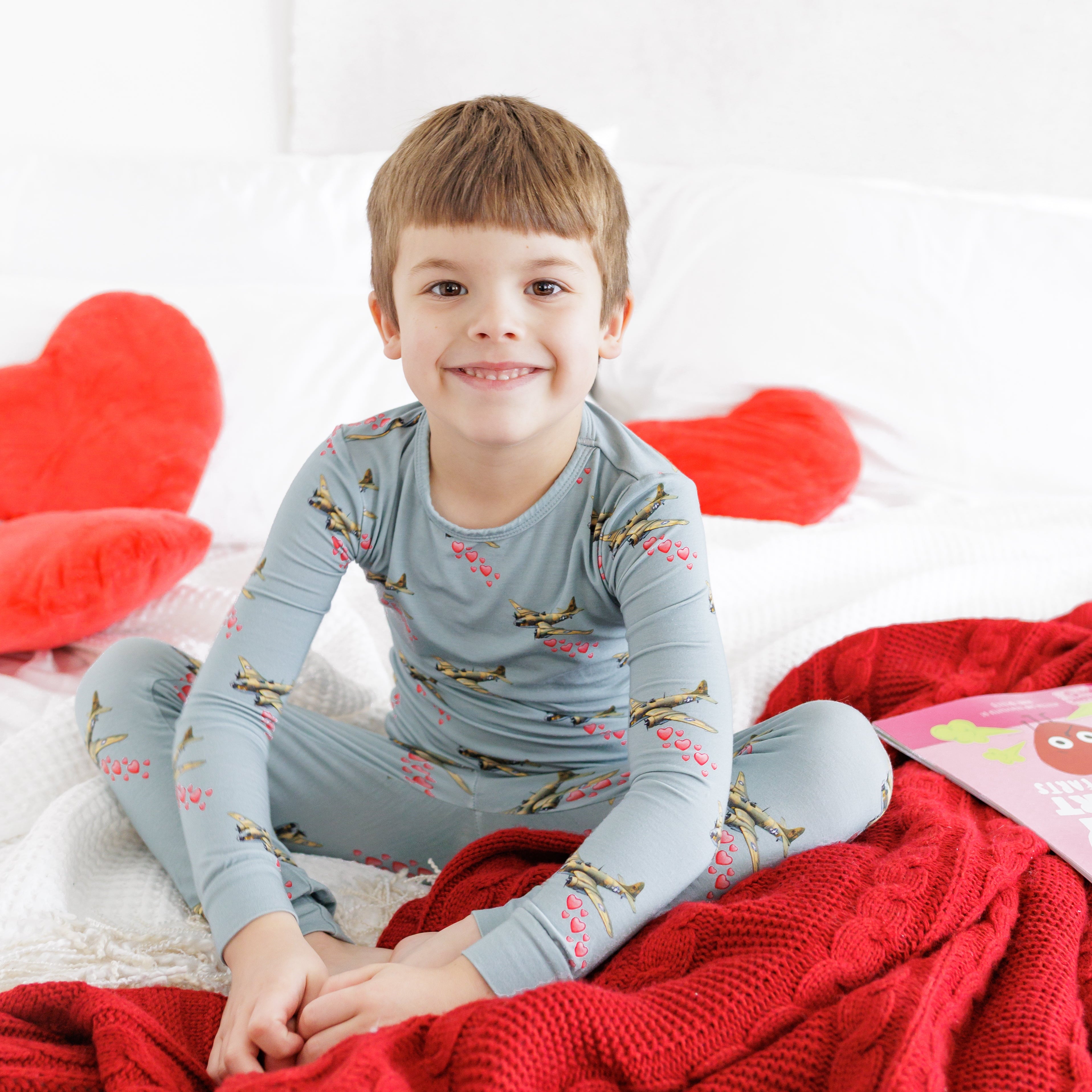 Child in pajamas sitting on a bed with red pillows and blanket