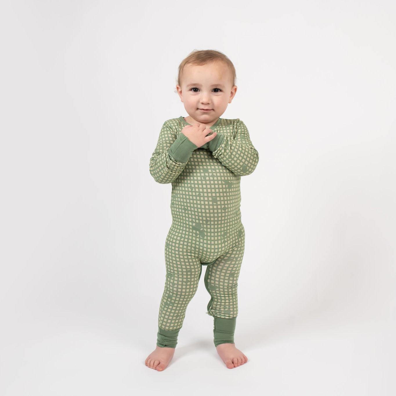Toddler standing on a white backdrop, wearing a sage green romper with a light tan grid pattern and matching green cuffs from 3rd Coast Limited