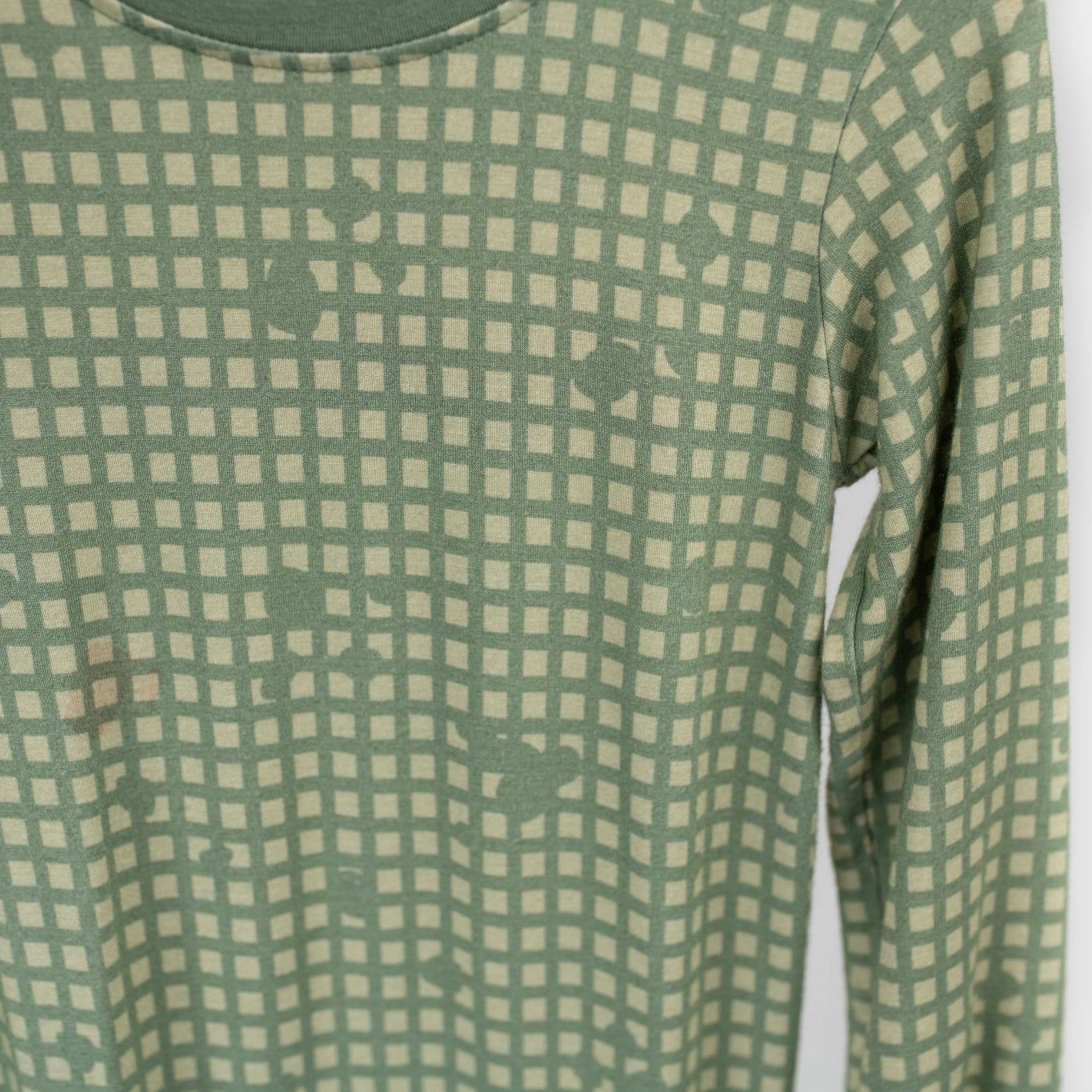 Close-up of sage green baby romper fabric with a subtle tan grid pattern and hidden tactical icons like pineapples, rifles, and helmets, designed by 3rd Coast Limited.