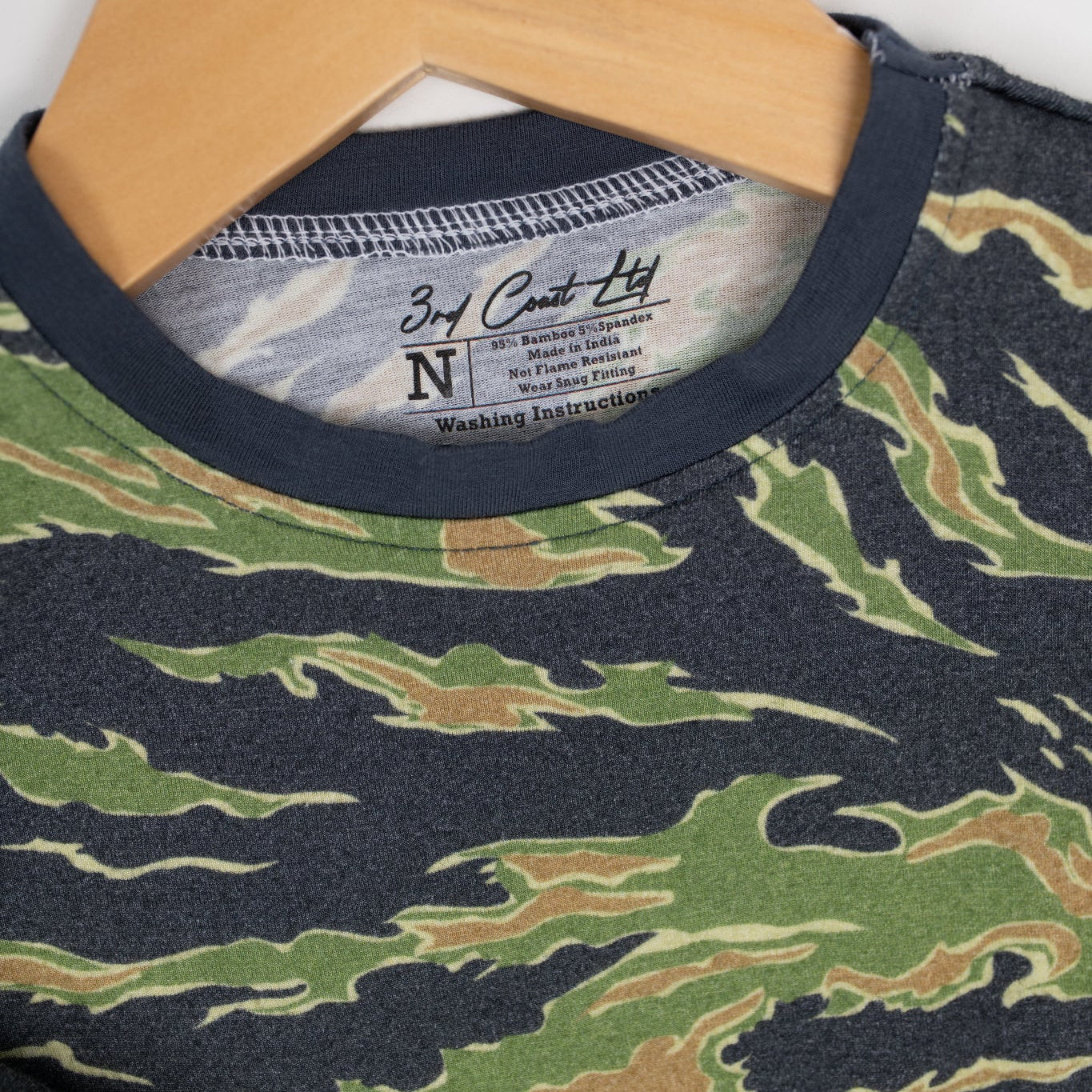 Close-up of a camo baby romper by 3rd Coast Limited, showing the green and brown tiger stripe pattern with navy trim and the inner neck label reading ‘95% Bamboo 5% Spandex – Made in India.