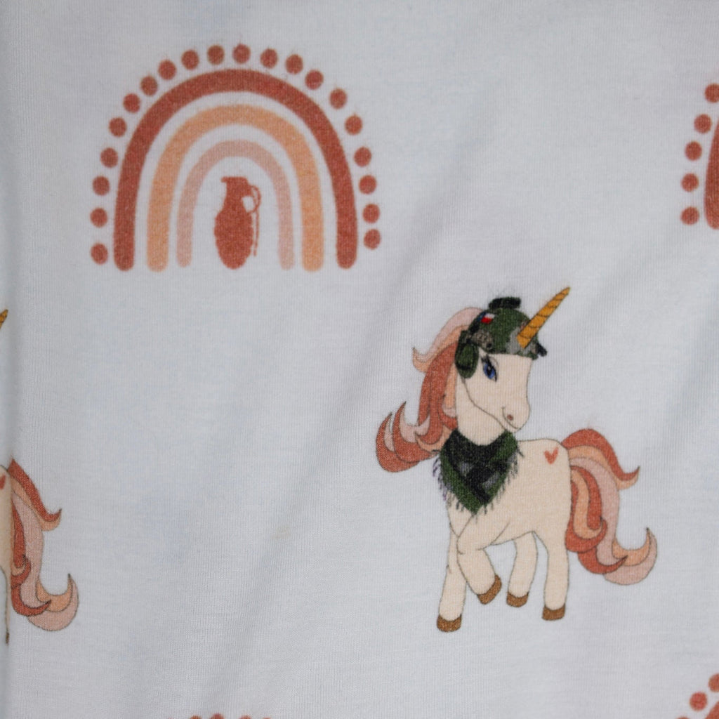 Close-up of cream baby romper fabric featuring a rust-colored rainbow with a grenade silhouette in the center and a tactical unicorn with a helmet and scarf, designed by 3rd Coast Limited.
