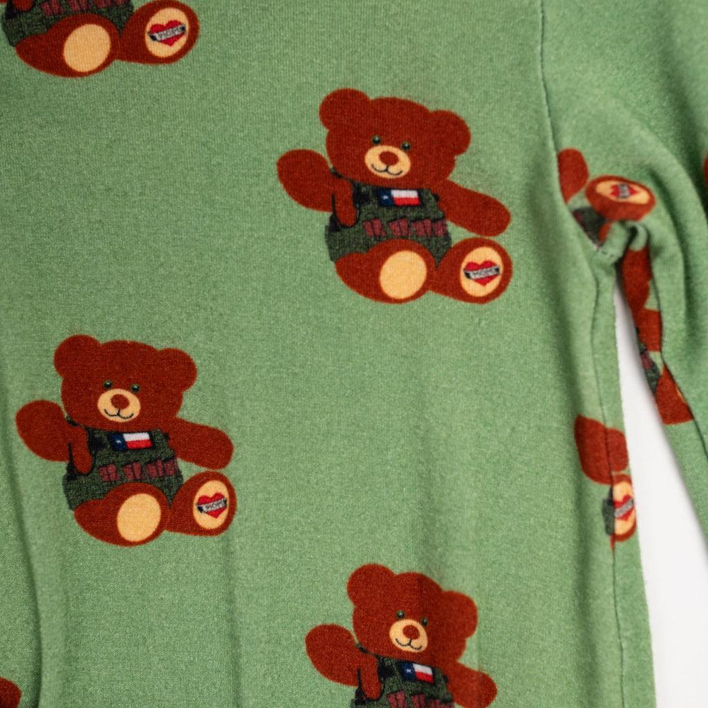 Close-up of green baby romper fabric featuring a repeating print of a brown tactical teddy bear wearing a vest with a Texas flag patch and a heart-shaped ‘Mom’ tattoo on its foot.